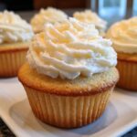 Close-up of a perfectly baked vanilla cupcake topped with a generous swirl of white buttercream frosting.