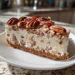 A thick slice of no-bake pecan cream pie showing a creamy filling studded with chopped pecans and topped with whole pecans.
