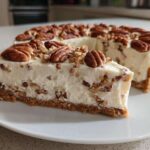 A slice of creamy, no-bake pecan cream pie sits on a white plate, topped with whole pecans.