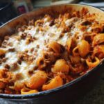 Close-up of a baked one pot enchilada pasta dish topped with melted, gooey cheese and rich meat sauce.