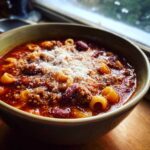 Close-up of a rustic bowl of pasta e fagioli soup topped generously with grated Parmesan cheese.