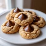 A stack of freshly baked peanut butter kiss cookies topped with melted chocolate kisses, ready to eat.