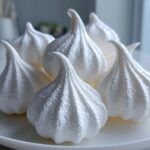 Close-up of several perfectly piped, crisp white meringue cookies arranged on a white plate.