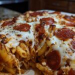 A close-up, mouth-watering shot of a baked pizza pasta casserole topped with melted mozzarella cheese, pepperoni slices, and herbs.
