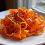 Close-up of vibrant orange ribbons in a raw carrot salad, topped generously with black and white sesame seeds.