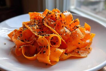 Close-up of vibrant orange ribbons in a raw carrot salad, topped generously with black and white sesame seeds.