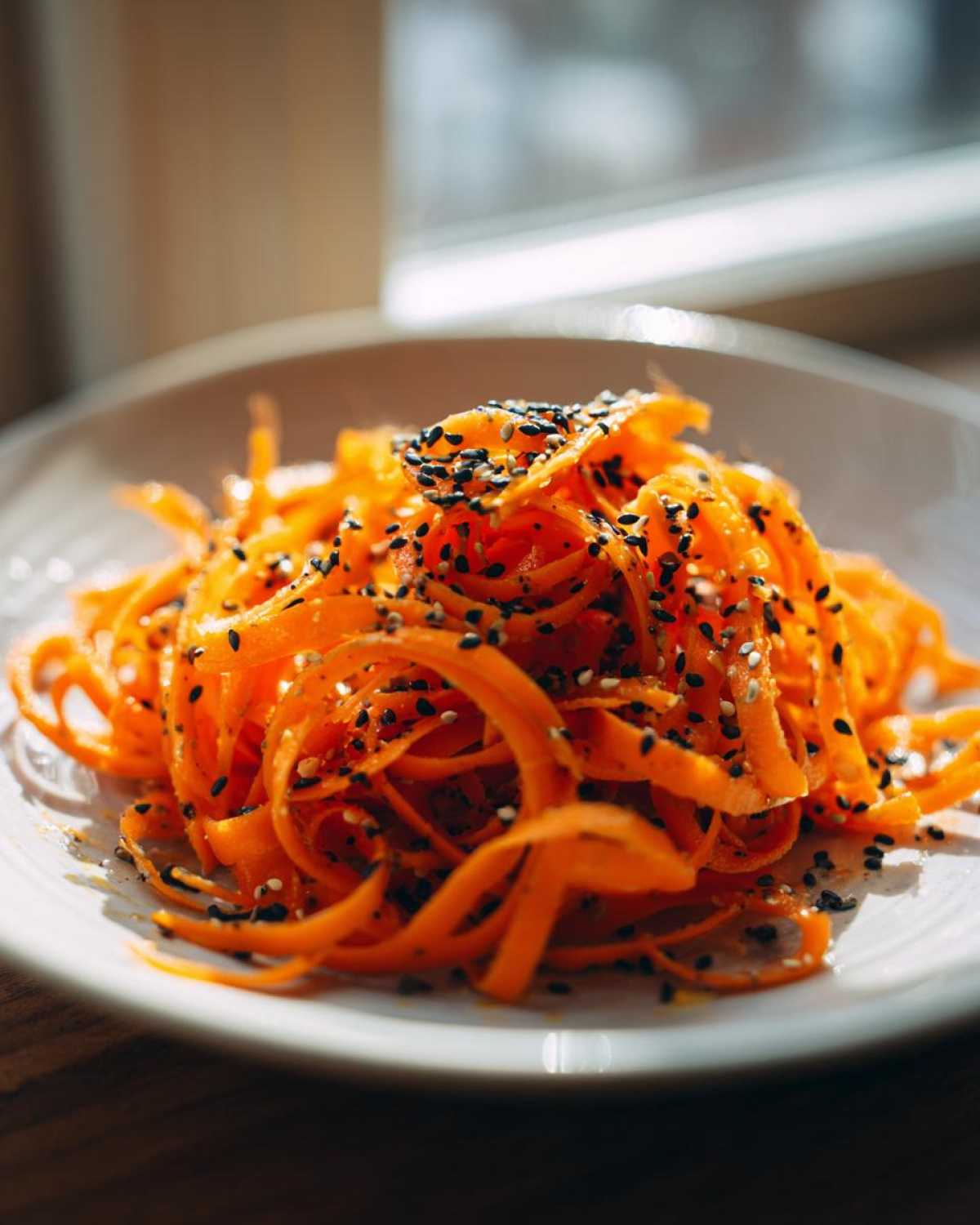 Close-up of a vibrant raw carrot salad made with spiralized carrots and topped generously with black and white sesame seeds.
