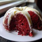 Close-up of a slice cut from a vibrant red velvet bundt cake topped with thick white cream cheese drizzle.