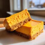 Close-up of two rich pumpkin cheesecake bars stacked slightly, showing the thick graham cracker crust.
