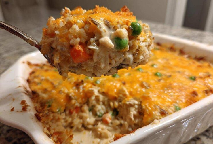 A spoonful of creamy chicken and wild rice casserole topped with melted cheddar cheese being lifted from the baking dish.