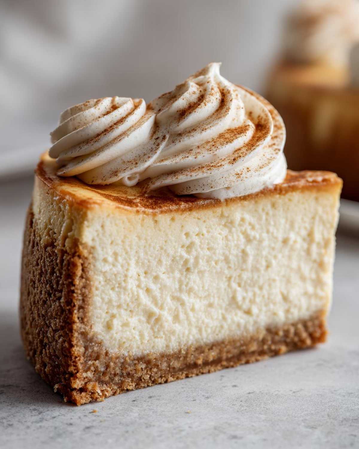 Close-up of a perfect slice of eggnog cheesecake recipe topped with piped whipped cream and cinnamon.