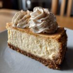 A close-up slice of creamy eggnog cheesecake recipe topped with piped whipped cream and cinnamon.