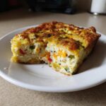A thick slice of vegetable egg bake with colorful peppers served on a white plate.