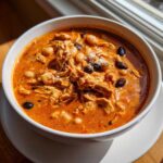 A close-up of a hearty bowl of slow cooker buffalo chicken chili with shredded chicken and mixed beans.