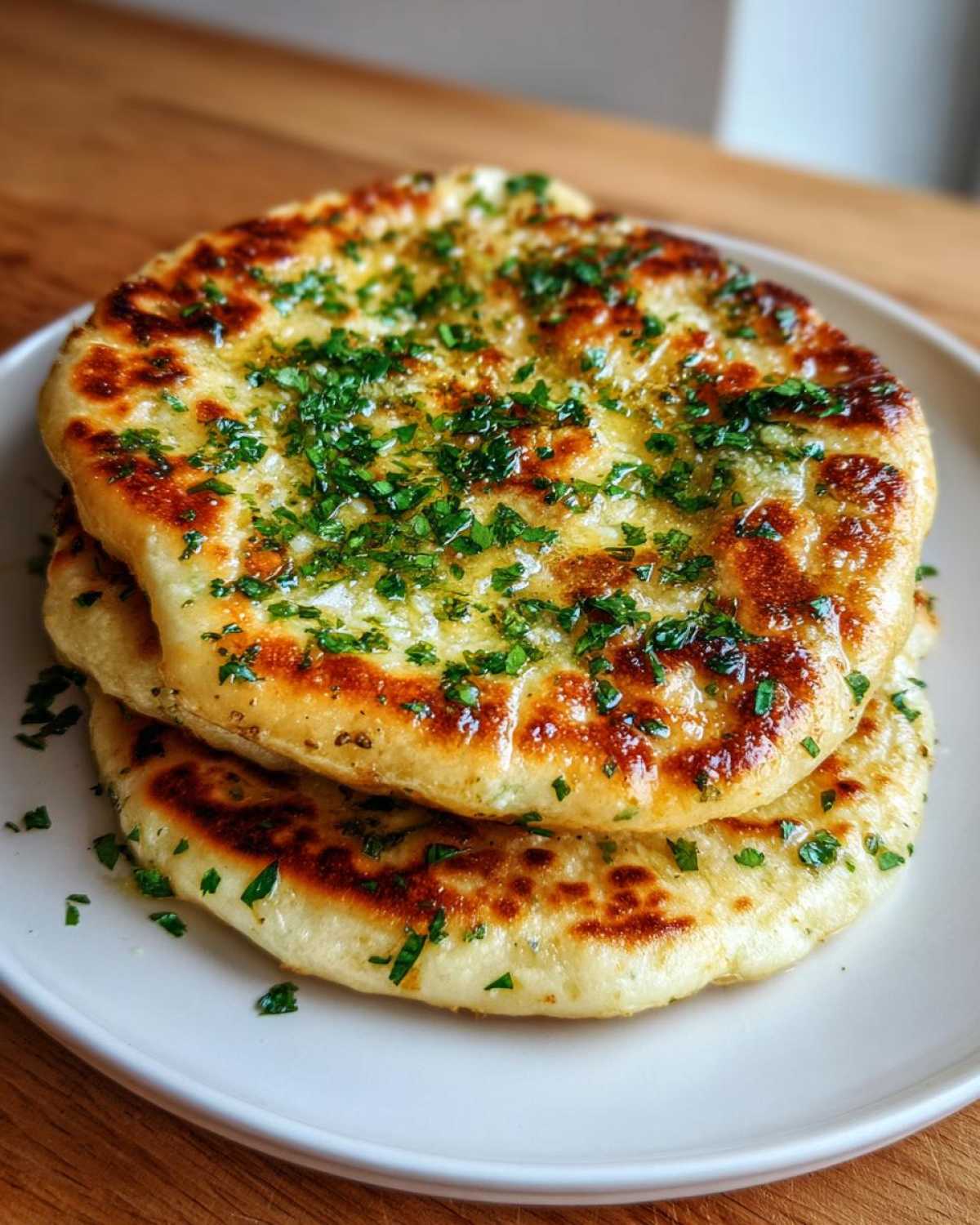 Two pieces of soft, golden naan bread brushed with melted butter and topped with fresh chopped parsley.