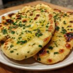 Close-up of three pieces of soft, golden naan bread brushed with melted butter and sprinkled with fresh parsley.