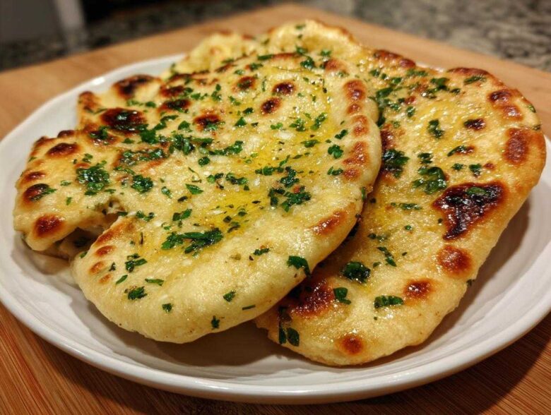 Close-up of three pieces of soft, golden naan bread brushed with melted butter and sprinkled with fresh parsley.
