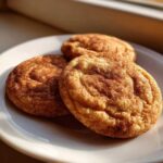 Three soft, chewy snickerdoodle cookies generously coated in cinnamon sugar, resting on a white plate.