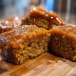 Close-up of rich, glazed squares of Southern candied yams resting on a wooden cutting board.
