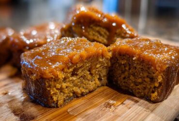 Close-up of rich, glazed squares of Southern candied yams resting on a wooden cutting board.