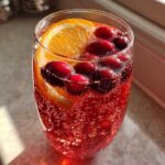 Close-up of a fizzy, red non-alcoholic christmas punch garnished with fresh cranberries and an orange slice.