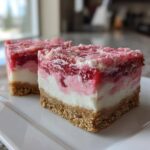 Two delicious squares of strawberry crunch cheesecake bars showing graham cracker crust, creamy filling, and strawberry topping.