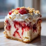 A close-up of a rich slice of strawberry shortcake cheesecake showing layers of creamy filling, strawberry swirls, and a graham cracker crust.