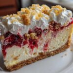 A decadent slice of strawberry shortcake cheesecake featuring a graham cracker crust, creamy filling, strawberry layer, whipped cream, and crumble topping.