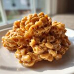 Mounds of sticky, golden-brown toffee chex mix recipe clusters piled on a white plate.