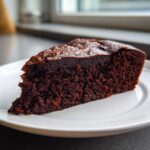 Close-up of a rich, dark slice of ultra moist chocolate cake resting on a white plate.