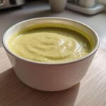 Close-up of a bowl of smooth, light green celery soup with tiny flecks, showcasing its velvet texture.