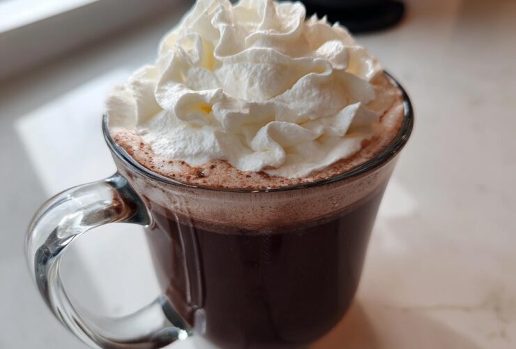 A clear glass mug filled with rich, dark whipped hot chocolate topped generously with fluffy whipped cream.