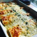 Close-up of baked white chicken enchiladas covered in melted, browned cheese and sprinkled with parsley.