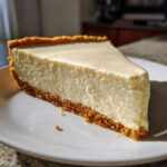 A thick, creamy slice of white chocolate cheesecake with a graham cracker crust on a white plate.