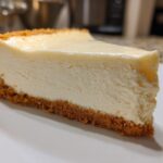A perfect slice of creamy white chocolate cheesecake with a thick graham cracker crust on a white plate.
