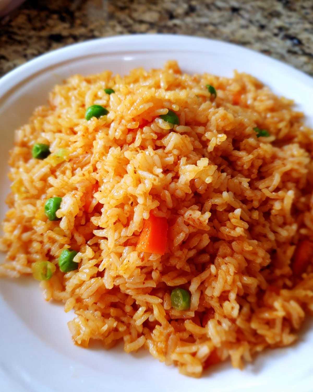 A close-up shot of vibrant, orange-colored spanish rice served on a white plate, mixed with bright green peas and diced carrots.