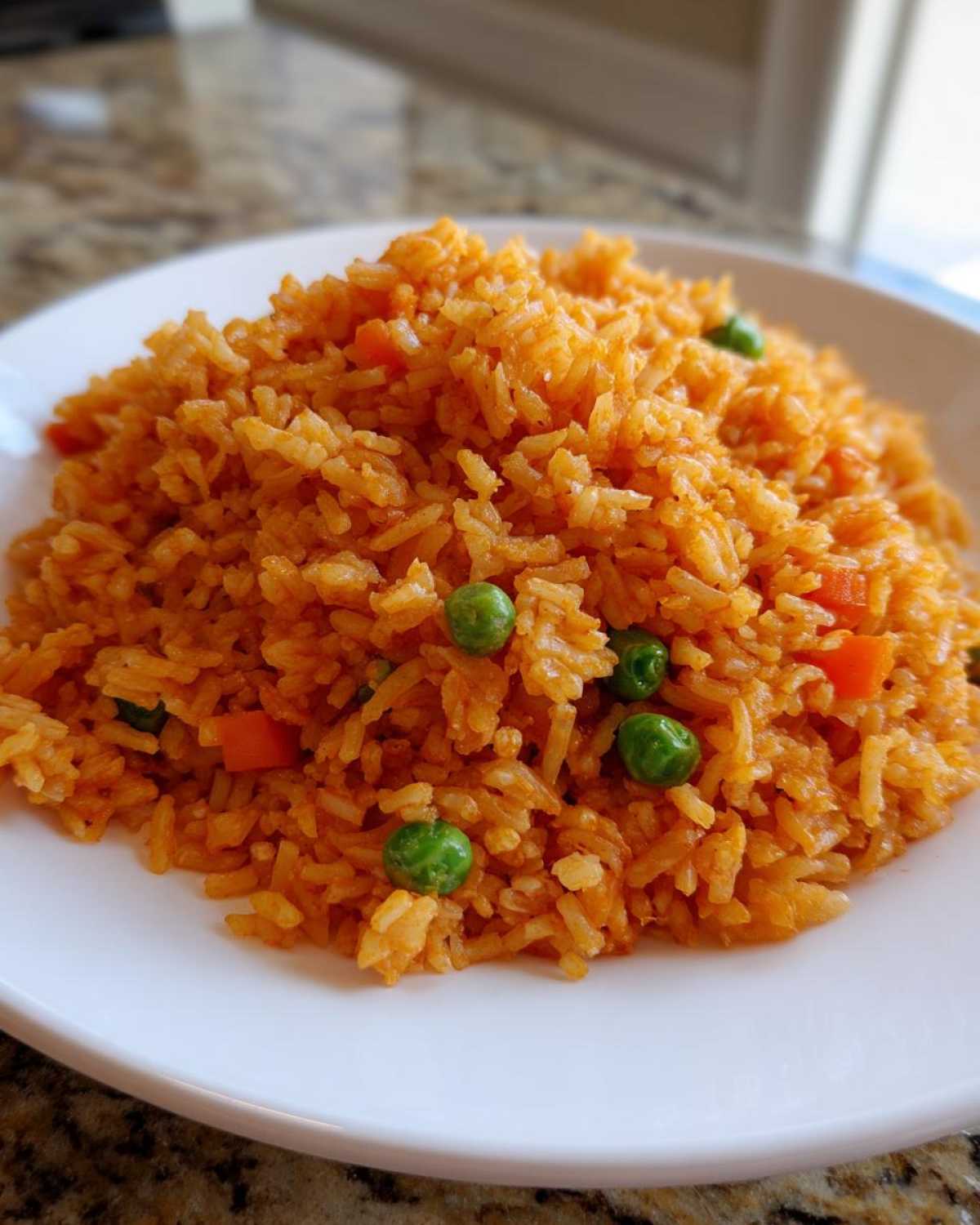 A close-up of a mound of vibrant orange spanish rice mixed with bright green peas and diced carrots on a white plate.
