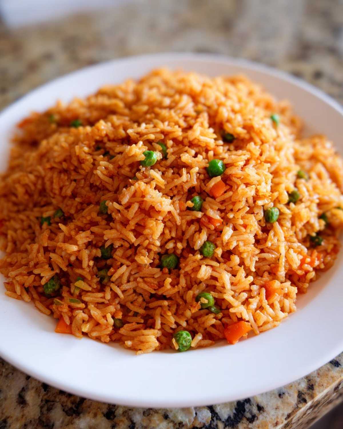 Close-up of a white plate piled high with vibrant orange Spanish rice mixed with green peas and diced carrots.