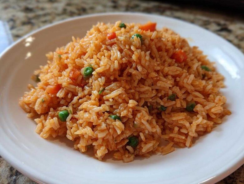 A close-up of fluffy, orange-red spanish rice mixed with bright green peas and diced carrots on a white plate.