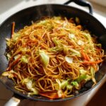 Close-up of freshly cooked, steaming fried noodles mixed with cabbage and carrots in a black wok.