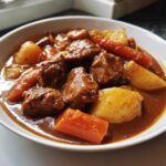 Close-up of a white bowl filled with rich, savory pork stew chunks, carrots, and potatoes.