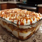 Close-up of a delicious caramel apple trifle layered in a glass dish, topped with whipped cream and caramel drizzle.