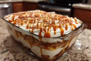 Close-up of a delicious caramel apple trifle layered in a glass dish, topped with whipped cream and caramel drizzle.