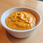 Close-up of a small white ramekin filled with thick, creamy orange beer cheese dip.