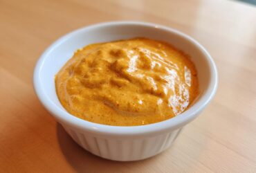 Close-up of a small white ramekin filled with thick, creamy orange beer cheese dip.