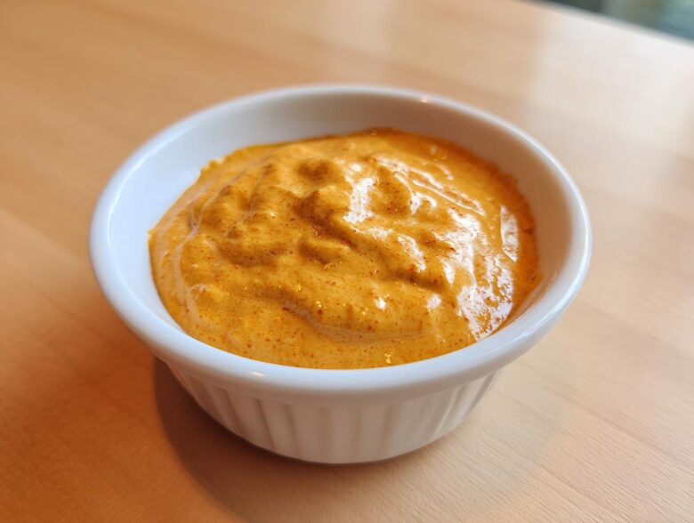 Close-up of a small white ramekin filled with thick, creamy orange beer cheese dip.
