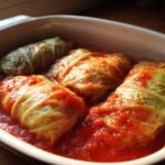 Three plump cabbage rolls simmering in a rich, red tomato sauce inside a white baking dish.
