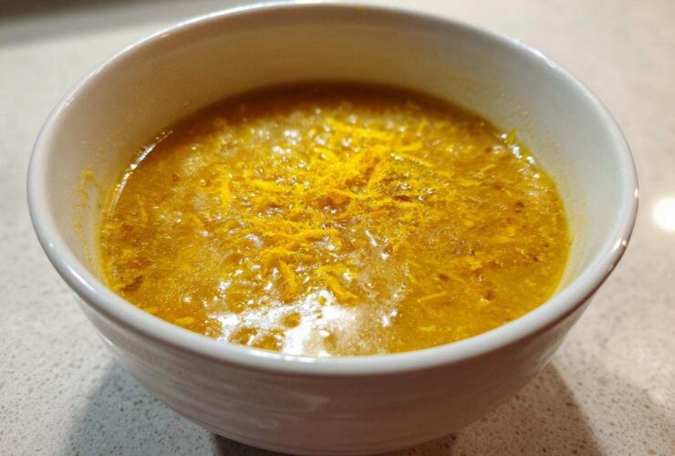 A close-up of a vibrant yellow chickpea soup garnished with orange zest in a white bowl.