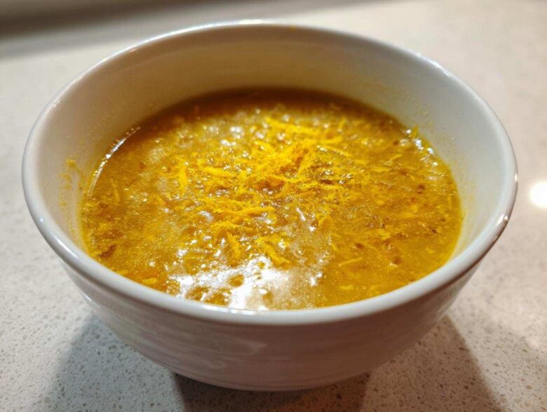 A close-up of a vibrant yellow chickpea soup garnished with orange zest in a white bowl.