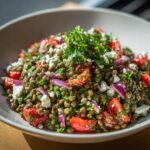 Close-up of a vibrant lentil salad mixed with chopped tomatoes, red onion, feta cheese, and fresh parsley.